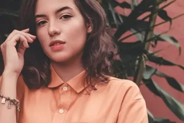 Girl with brown hair and orange shirt with trees in the background